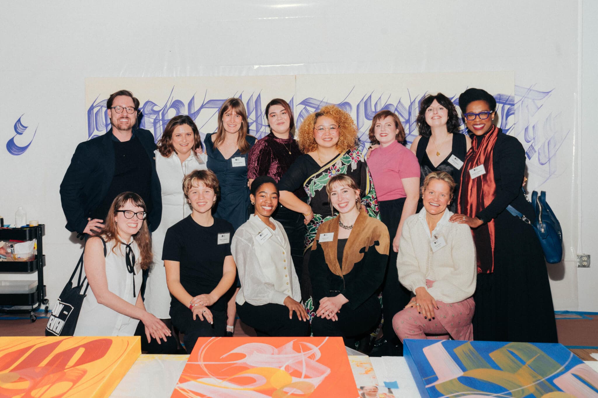 Boston Art Review Editorial Team posing in two tiers behind a table sporting some of Shrestha's work, and in front of a banner with her design.