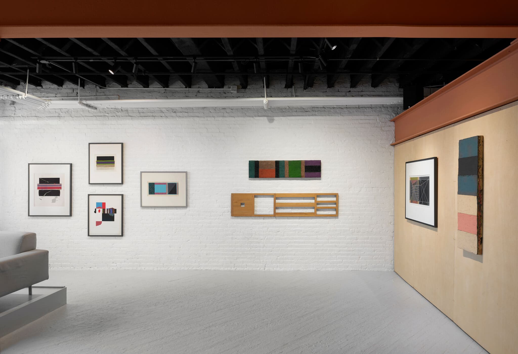 An installation view of "The Rob Moore Retrospective" at Gallery VERY in Boston. Seven abstract paintings by the artist line the wall featuring shades of blue, red, and green.